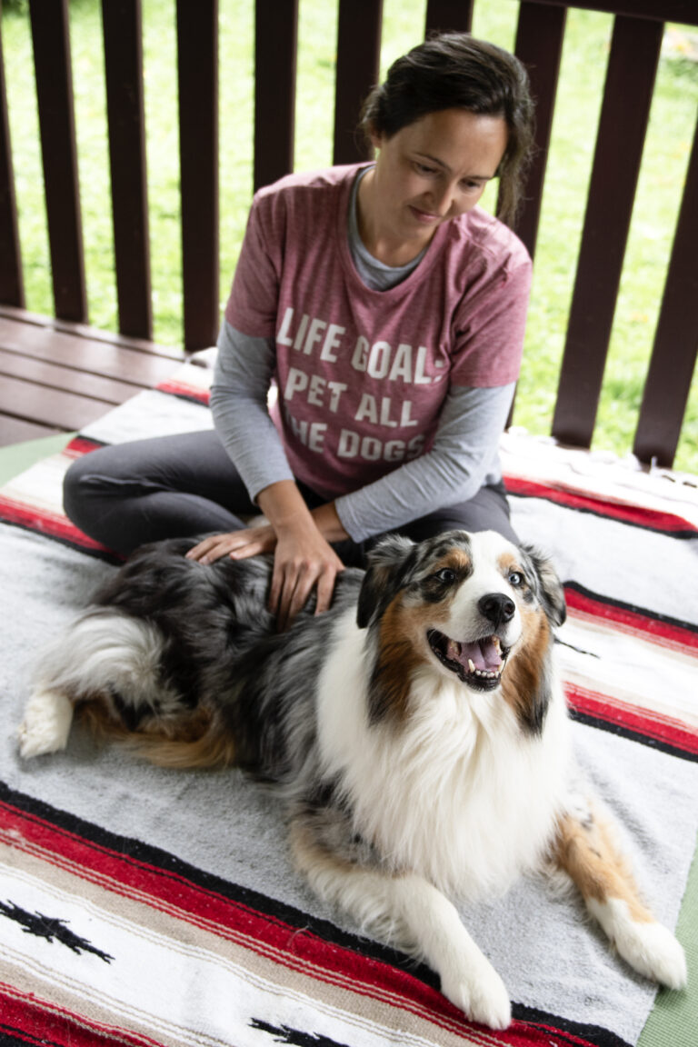 Woman sitting on the ground proving animal massage to a dog