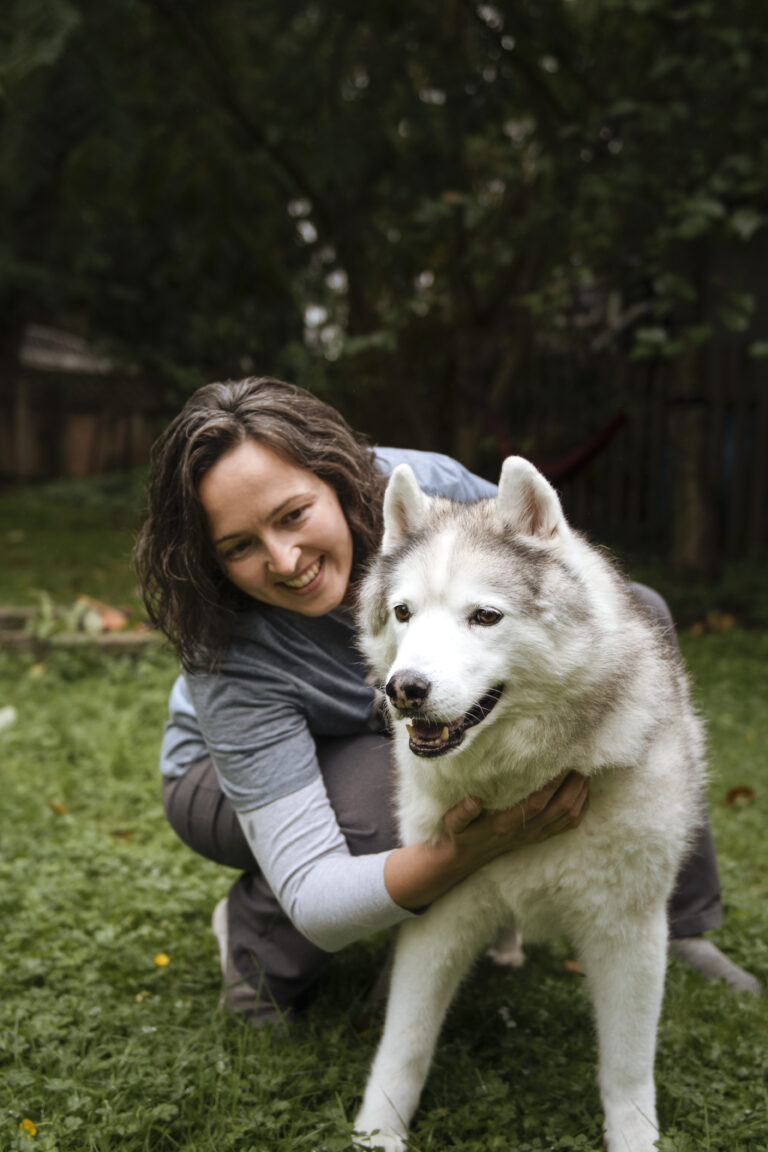 Woman crouched in the grass hugging a Siberian Husky